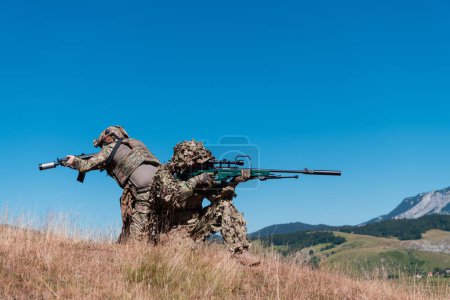 Téléchargez les photos : Une équipe de tireurs d'élite de soldats est infiltrée. Assistante de sniper et chef d'équipe marchant et visant dans la nature avec herbe jaune et ciel bleu. Uniforme de camouflage tactique - en image libre de droit