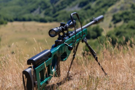 Photo for A green military sniper rifle with a scope for long distance tactical modern warfare in yellow grass blue sky. - Royalty Free Image