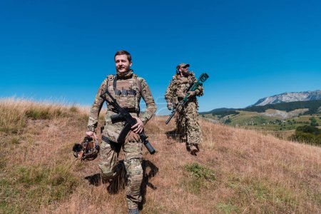 Photo for A sniper team squad of soldiers is going undercover. Sniper assistant and team leader walking and aiming in nature with yellow grass and blue sky. Tactical camouflage uniform - Royalty Free Image