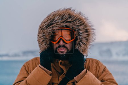 Kopfballfoto eines Mannes in einer kalten, verschneiten Gegend mit dicker brauner Winterjacke, Schneebrille und Handschuhen. Das Leben in kalten Regionen des Landes
