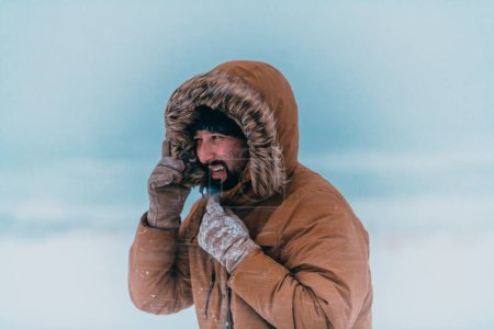 Photo for Headshot photo of a man in a cold snowy area wearing a thick brown winter jacket and gloves. Life in cold regions of the country - Royalty Free Image
