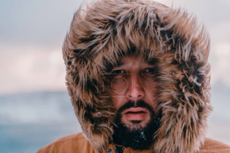 Foto de Foto de un hombre en una zona nevada fría con una gruesa chaqueta de invierno marrón y guantes. La vida en las regiones frías del país - Imagen libre de derechos