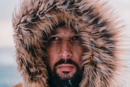Téléchargez les photos : Photo de tête d'un homme dans une zone enneigée froide portant une épaisse veste d'hiver brune et des gants. La vie dans les régions froides du pays - en image libre de droit
