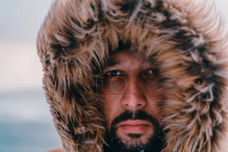 Foto de Foto de un hombre en una zona nevada fría con una gruesa chaqueta de invierno marrón y guantes. La vida en las regiones frías del país - Imagen libre de derechos