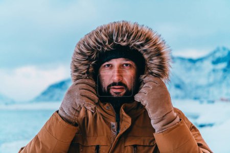 Photo for Headshot photo of a man in a cold snowy area wearing a thick brown winter jacket and gloves. Life in cold regions of the country - Royalty Free Image