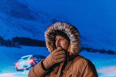 Téléchargez les photos : Prise de vue d'un homme dans une zone enneigée froide portant une épaisse veste d'hiver brune, des lunettes de neige et des gants lors d'une froide nuit scandinave. La vie dans les régions froides du pays - en image libre de droit