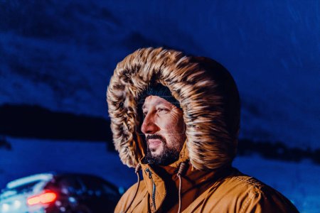 Photo for Head shot of a man in a cold snowy area wearing a thick brown winter jacket, snow goggles and gloves on a cold Scandinavian night. Life in the cold regions of the country - Royalty Free Image