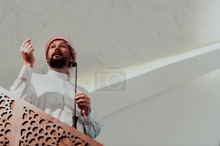 Foto de Musulmanes imán árabe tiene un discurso el viernes por la tarde la oración en la mezquita. Los musulmanes se han reunido para la oración del viernes por la tarde en la mezquita y están escuchando el discurso del imán. - Imagen libre de derechos