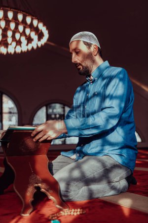 Téléchargez les photos : Un musulman lit le saint livre islamique Coraqn dans une grande mosquée moderne pendant le mois sacré musulman de Ranazan. - en image libre de droit