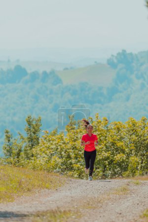 Foto de Joven mujer feliz disfrutando de un estilo de vida saludable mientras trota en un camino rural a través del hermoso bosque soleado, el ejercicio y el concepto de fitness
. - Imagen libre de derechos