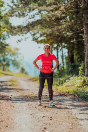 Téléchargez les photos : Jeune femme heureuse jouissant d'un mode de vie sain tout en faisant du jogging sur une route de campagne à travers la belle forêt ensoleillée, concept d'exercice et de remise en forme
. - en image libre de droit