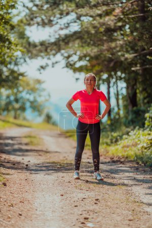 Foto de Joven mujer feliz disfrutando de un estilo de vida saludable mientras trota en un camino rural a través del hermoso bosque soleado, el ejercicio y el concepto de fitness
. - Imagen libre de derechos