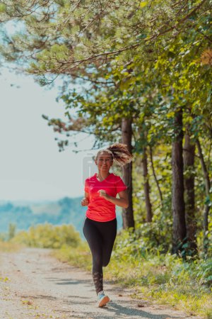 Photo for Young happy woman enjoying in a healthy lifestyle while jogging on a country road through the beautiful sunny forest, exercise and fitness concept. - Royalty Free Image