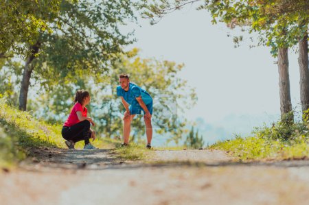 Téléchargez les photos : A young couple resting after an exhausting run in the early morning on an idyllic forest road. - en image libre de droit