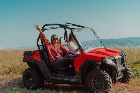Téléchargez les photos : Deux jeunes femmes heureuses et excitées profitant d'une belle journée ensoleillée tout en conduisant une voiture tout terrain buggy sur la montagne nature. - en image libre de droit