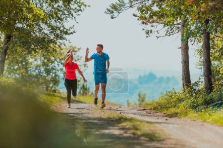 Photo for Couple enjoying in a healthy lifestyle while jogging on a country road through the beautiful sunny forest, exercise and fitness concept. - Royalty Free Image