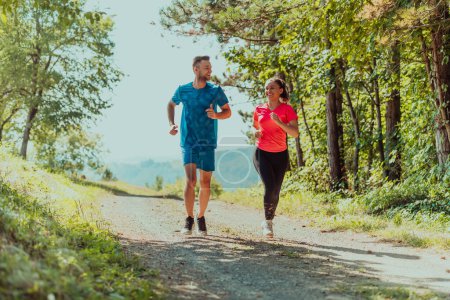 Photo for Couple enjoying in a healthy lifestyle while jogging on a country road through the beautiful sunny forest, exercise and fitness concept. - Royalty Free Image
