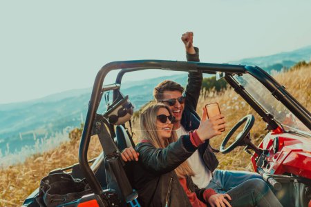 Photo for Young happy excited couple enjoying beautiful sunny day taking selfie picture while driving a off road buggy car on mountain nature. - Royalty Free Image