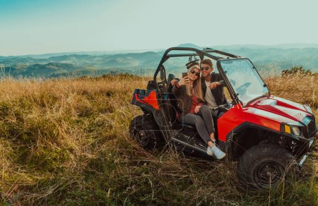 Téléchargez les photos : Jeune couple heureux et excité profitant d'une belle journée ensoleillée en prenant des photos selfie tout en conduisant une voiture tout terrain buggy sur la montagne nature. - en image libre de droit