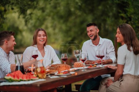 Foto de Grupo de amigos felices teniendo picnic francés cena al aire libre durante las vacaciones de verano cerca del río en la hermosa naturaleza. - Imagen libre de derechos