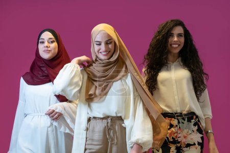 Téléchargez les photos : Portrait de groupe de belles femmes musulmanes deux d'entre eux en robe à la mode avec hijab isolé sur fond rose représentant la mode islam moderne et concept de Ramadan Kareem
. - en image libre de droit