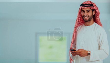 Téléchargez les photos : Young modern Muslim Arabian businessmen wearing traditional clothes while using smartphones at home - en image libre de droit