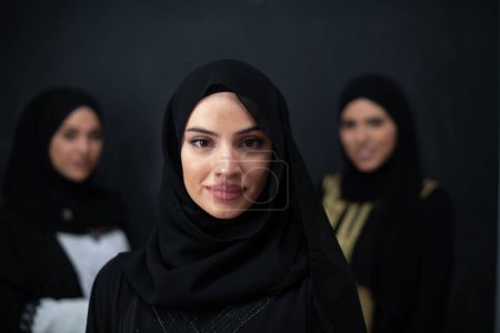 Téléchargez les photos : Group portrait of beautiful Muslim women in a fashionable dress with hijab isolated on black background. - en image libre de droit