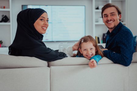 Téléchargez les photos : Happy Muslim family with daughter woman in traditional fashionable dress having fun and good time together while sitting on sofa. - en image libre de droit