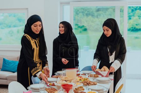 Téléchargez les photos : La famille musulmane de l'Aïd Moubarak dîne avec des jeunes filles musulmanes qui servent de la nourriture sur la table pendant le mois de fête du Ramadan à la maison. La famille islamique halal manger et boire islamique
. - en image libre de droit
