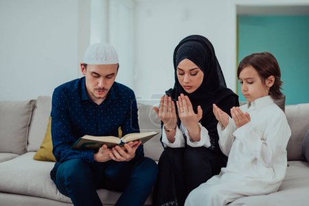 Photo for Happy Muslim family enjoying the holy month of Ramadan while praying and reading the Quran together in a modern home. - Royalty Free Image