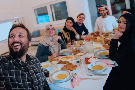 Photo for Eid Mubarak Muslim family having Iftar dinner taking pictures with smartphone while eating traditional food during Ramadan feasting month at home. The Islamic Halal Eating and Drinking Islamic family - Royalty Free Image