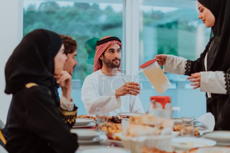 Foto de Muslim family having Iftar dinner drinking water to break feast. Eating traditional food during Ramadan feasting month at home. The Islamic Halal Eating and Drinking in modern home. - Imagen libre de derechos