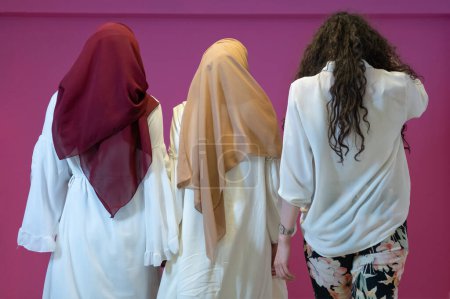 Téléchargez les photos : Portrait de groupe de belles femmes musulmanes deux d'entre eux en robe à la mode avec hijab isolé sur fond rose représentant la mode islam moderne et concept de Ramadan Kareem
. - en image libre de droit
