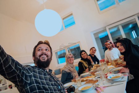 Téléchargez les photos : Eid Mubarak Muslim family having Iftar dinner taking pictures with smartphone while eating traditional food during Ramadan feasting month at home. The Islamic Halal Eating and Drinking Islamic family - en image libre de droit