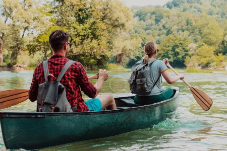 Photo for Couple adventurous explorer friends are canoeing in a wild river surrounded by the beautiful nature. - Royalty Free Image