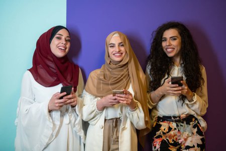 Téléchargez les photos : Portrait de groupe de belles femmes musulmanes deux d'entre eux en robe à la mode avec hijab isolé sur fond coloré représentant la mode islam moderne et le concept de Ramadan Kareem
. - en image libre de droit