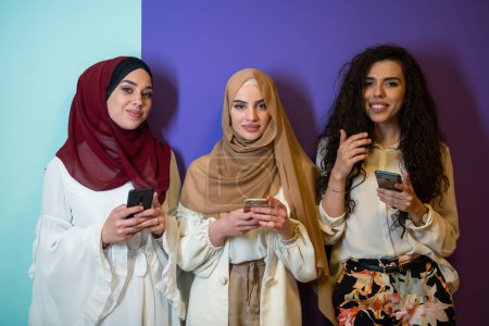 Téléchargez les photos : Portrait de groupe de belles femmes musulmanes deux d'entre eux en robe à la mode avec hijab isolé sur fond coloré représentant la mode islam moderne et le concept de Ramadan Kareem
. - en image libre de droit