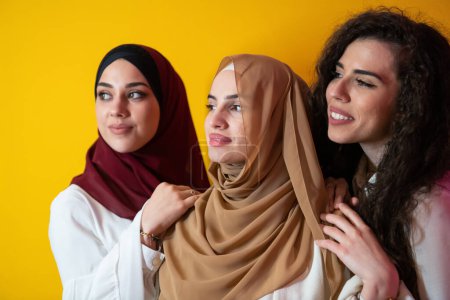 Téléchargez les photos : Portrait de groupe de belles femmes musulmanes deux d'entre elles dans une robe à la mode avec hijab isolé sur un fond jaune. Photo de haute qualité - en image libre de droit