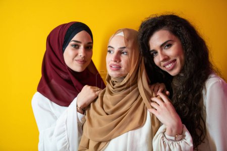 Photo for Group portrait of beautiful Muslim women two of them in a fashionable dress with hijab isolated on a yellow background. High quality photo - Royalty Free Image