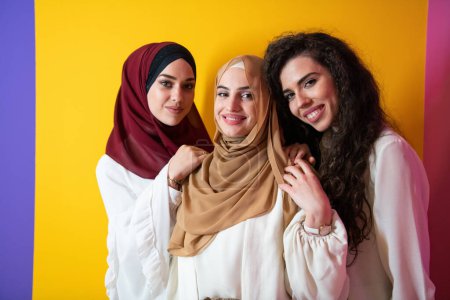 Téléchargez les photos : Portrait de groupe de belles femmes musulmanes deux d'entre elles dans une robe à la mode avec hijab isolé sur un fond jaune. Photo de haute qualité - en image libre de droit