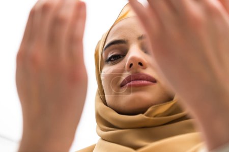 Téléchargez les photos : Portrait of beautiful muslim woman in fashionable dress with hijab making traditional prayer to God keeps hands in praying gesture isolated on white background. - en image libre de droit