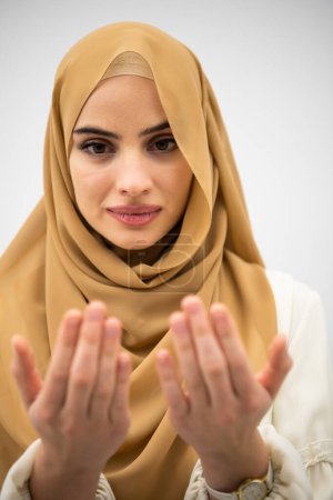 Téléchargez les photos : Portrait of beautiful muslim woman in fashionable dress with hijab making traditional prayer to God keeps hands in praying gesture isolated on white background. - en image libre de droit