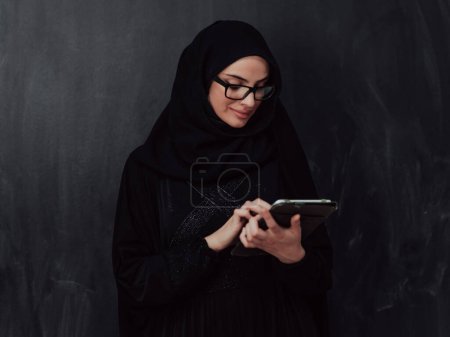 Téléchargez les photos : Jeune femme d'affaires musulmane moderne utilisant un smartphone portant des vêtements en hijab devant un tableau noir. - en image libre de droit