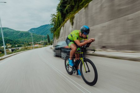 Téléchargez les photos : Full length portrait of an active triathlete in sportswear and with a protective helmet riding a bicycle. Selective focus . - en image libre de droit