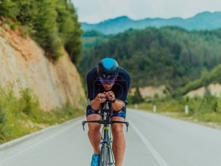 Photo for Full length portrait of an active triathlete in sportswear and with a protective helmet riding a bicycle. Selective focus . - Royalty Free Image