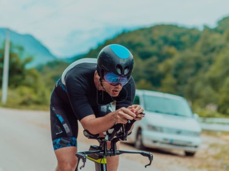 Foto de Full length portrait of an active triathlete in sportswear and with a protective helmet riding a bicycle. Selective focus . - Imagen libre de derechos