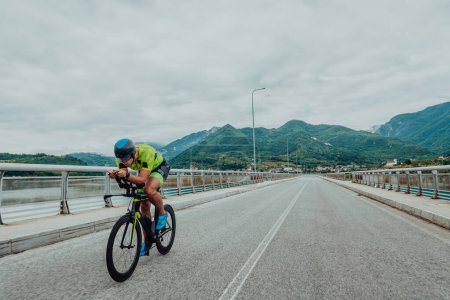 Photo for Full length portrait of an active triathlete in sportswear and with a protective helmet riding a bicycle. Selective focus . - Royalty Free Image