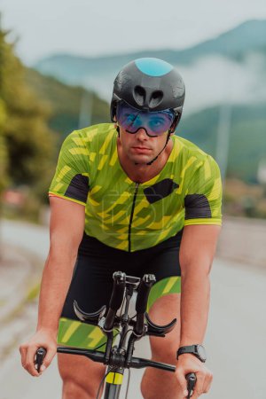 Foto de Active triathlete in sportswear and with a protective helmet riding a bicycle. Selective focus . - Imagen libre de derechos