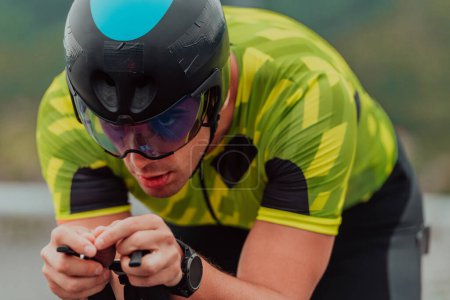 Foto de Close up photo of an active triathlete in sportswear and with a protective helmet riding a bicycle. Selective focus. - Imagen libre de derechos