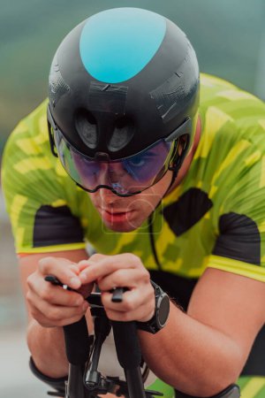 Foto de Close up photo of an active triathlete in sportswear and with a protective helmet riding a bicycle. Selective focus. - Imagen libre de derechos